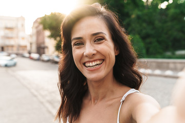 Portrait of pretty woman smiling and taking selfie photo on city street