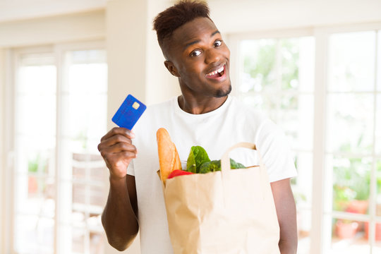 African american man holding paper bag full of groceries and holding credit card as payment