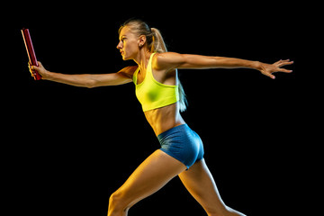 Professional female relay racer training isolated on black studio background in neon light. Woman...