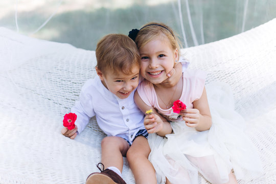 Cute little sister and brother having fun together in hammock in green summer garden, hugging and smiling. Happiness, childhood, summer time concept
