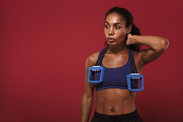 Fototapeta na wymiar Serious strong young african fitness sports woman posing isolated over red wall background posing with expander.