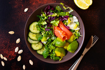 Healthy dietary salad with salmon, avocado, pumpkin seeds, fresh vegetables and lemon. The concept of healthy eating. Dark background, top view, copy space
