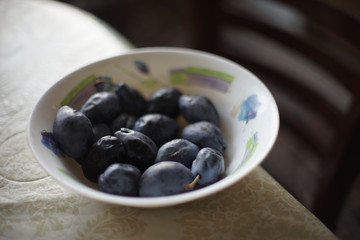 Blue plums lie in a deep white plate on the table.