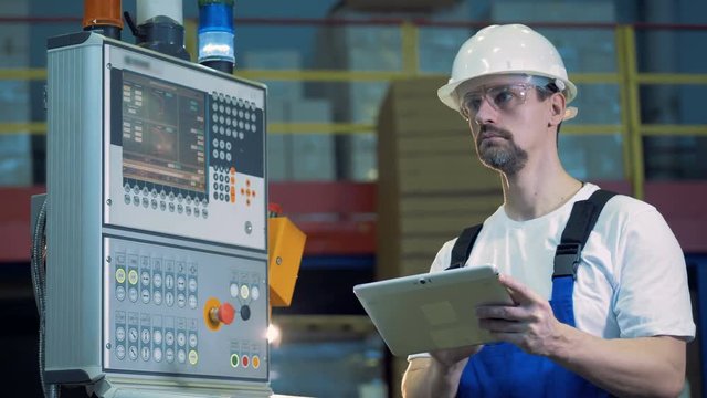 Male engineer with a tablet is standing near the control board