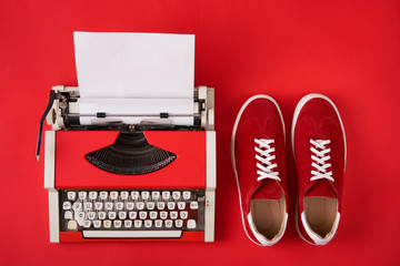 Red suede sneakers shoes and typewriter with blank paper sheet on red background