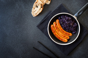 Roasted sausages bratwurst served in pan with bread and red cabbage on a black background. Traditional German dish, German cuisine. Top view, copy space