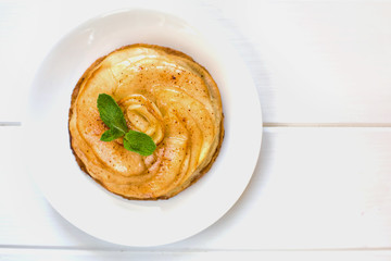 Round cake made from apple charlotte with mint leaves close up on a white wooden background...