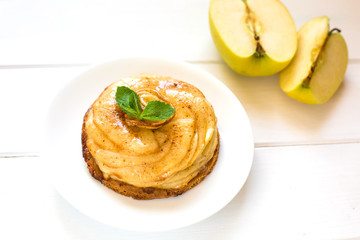 A round apple pie pie with mint leaves close up on a white wooden background and a sliced apple.