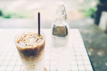 Iced coffee espresso in a tall glass on white table beside water bottle vintage style