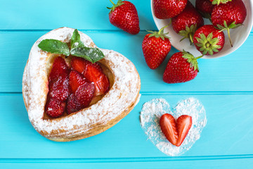 Heart-shaped cake with strawberries and mint on a bright blue background, on which are fresh strawberries and a heart of powdered sugar