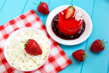 Red round cake with strawberry souffle, decorated with mint leaves on a plate, which stands on a blue wooden background. Nearby is a plate with cottage cheese and strawberries.