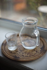 Jug of water and a glass in a tray on the windowsill
