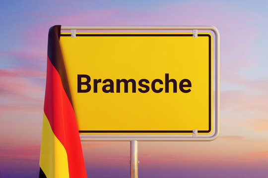 Bramsche. Gelbes Schild/Ortsschild. Flagge von Deutschland h&auml;ngt dar&uuml;ber. Himmel mit Sonnenuntergang oder Sonnenaufgang