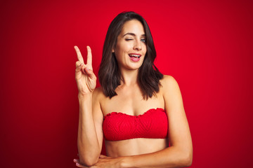 Beautiful woman wearing bikini swimwear over red isolated background smiling with happy face...