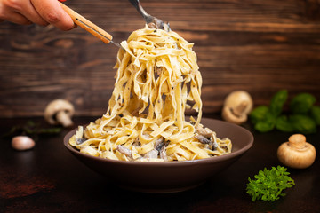 Homemade Italian fettuccine pasta with mushrooms and cream sauce (Fettuccine al Funghi Porcini). Traditional Italian cuisine. Served on a dark table with a rustic wooden background. Close-up