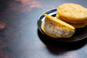 Latin American breakfast Arepas (arepa) of ground maize dough with cheese and herbs. Cuisine of Venezuela and Colombia. Close-up view, dark background, copy space