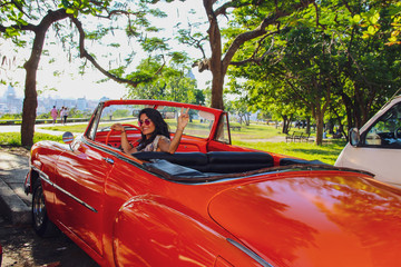 girl driving old orange car in Havana, Cuba