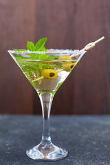 alcoholic cocktail with liqueur in a high glass with a sugar edge with olives and mint on a dark concrete background 