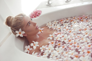 Obraz na płótnie Canvas Spa Relax. Blonde enjoying bath with plumeria tropical flowers. Health And Beauty. Closeup Beautiful Sexy Girl Bathing With Petals. Treatment, Aromatherapy Skin Body Care Therapy.