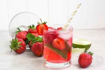 strawberry cocktail in a glass with ice and mint, a bowl with strawberries and lime slices