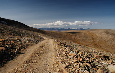 Road through a dry stone desert steppe on a highland mountain plateau with yellow green grass with ranges of hills rocks on a horizon skyline