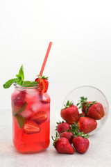 On a light background there is a strawberry cocktail in a glass with ice and mint, a bowl with strawberries