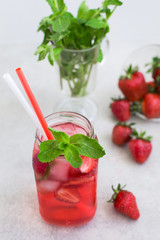 On a light background there is a strawberry cocktail in a glass with ice and mint, a bowl with strawberries 