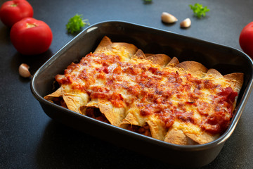 Mexican enchiladas with chicken, vegetables, corn, beans, tomato sauce and cheese. Served in baking tray. Mexican food. Latin American cuisine. Black background, close-up, copy space