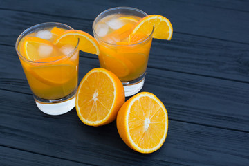  Alcoholic and non-alcoholic citrus drink with orange and lemon in glasses on a dark wooden background