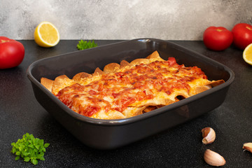 Mexican Enchiladas with chicken, vegetables, corn, beans and cheese. Served in a baking tray on a black table. Mexican food. Latin American cuisine. Gray background, close up, copy space
