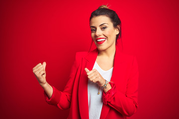 Young beautiful business woman standing over red isolated background Pointing to the back behind with hand and thumbs up, smiling confident