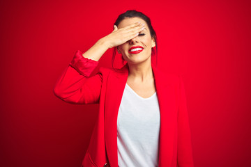 Young beautiful business woman standing over red isolated background smiling and laughing with hand on face covering eyes for surprise. Blind concept.