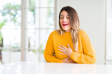 Young beautiful woman wearing winter sweater at home Smiling and laughing hard out loud because funny crazy joke. Happy expression.