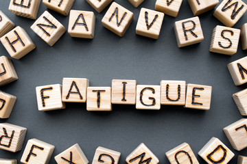 word fatigue composed of wooden cubes with letters, weakness extremely tired concept, scattered around the cubes random letters, top view on gray background