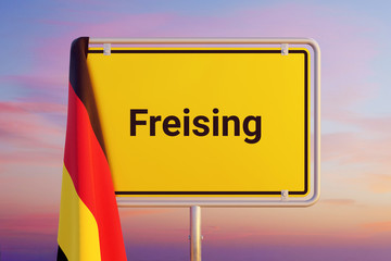 Freising. Gelbes Schild/Ortsschild. Flagge von Deutschland hängt darüber. Himmel mit Sonnenuntergang oder Sonnenaufgang