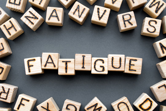 word fatigue composed of wooden cubes with letters, weakness extremely tired concept, scattered around the cubes random letters, top view on gray background