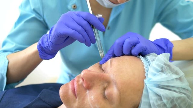The concept of contour plastic face. A plastic surgeon's hand puts a filler injection in the face of a woman. close-up