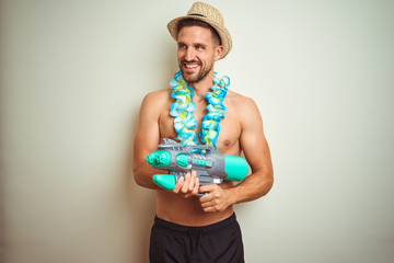 Handsome shirtless man wearing hawaiian lei and water gun over background with a happy face...