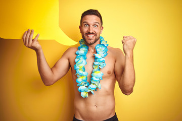 Handsome shirtless man wearing hawaiian lei holding speech bubble over yellow background screaming...