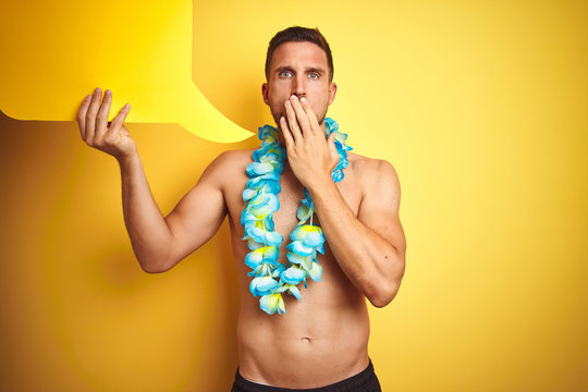 Handsome shirtless man wearing hawaiian lei holding speech bubble over yellow background cover mouth with hand shocked with shame for mistake, expression of fear, scared in silence, secret concept