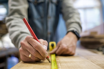 Carpenter measuring and tracing lines with a ruler on a wooden surface. Close up view. Blurred...