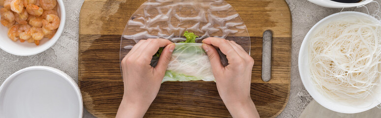 panoramic shot of woman making roll on cutting board among ingredients