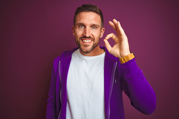 Young fitness man wearing casual sports sweatshirt over purple isolated background smiling positive doing ok sign with hand and fingers. Successful expression.