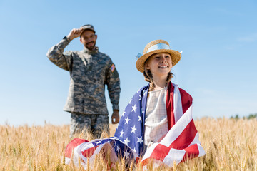 selective focus of cheerful kid standing with american flag near soldier