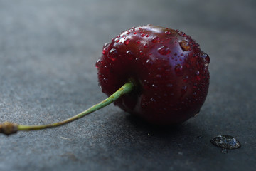 red juicy cherries in drops of water against a dark background