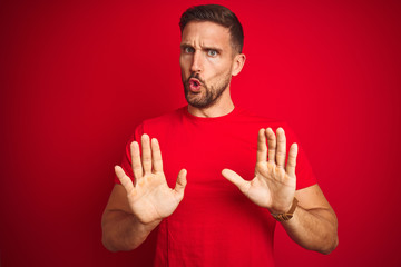 Young handsome man wearing casual t-shirt over red isolated background Moving away hands palms showing refusal and denial with afraid and disgusting expression. Stop and forbidden.