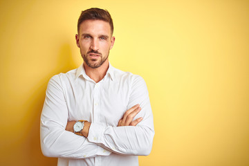 Young handsome man wearing elegant white shirt over yellow isolated background skeptic and nervous, disapproving expression on face with crossed arms. Negative person.