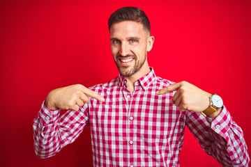 Young handsome man over red isolated background looking confident with smile on face, pointing...