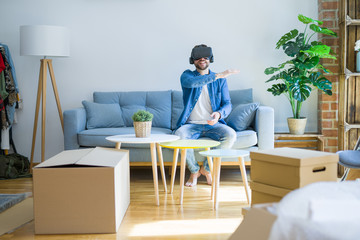 Young man wearing virtual reality glasses playing a simulation game sitting on the sofa around cardboard boxes moving to a new house