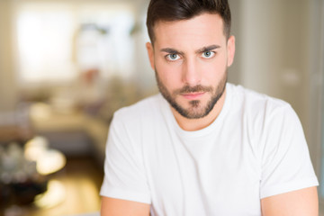 Young handsome man wearing casual white t-shirt at home skeptic and nervous, disapproving expression on face with crossed arms. Negative person.